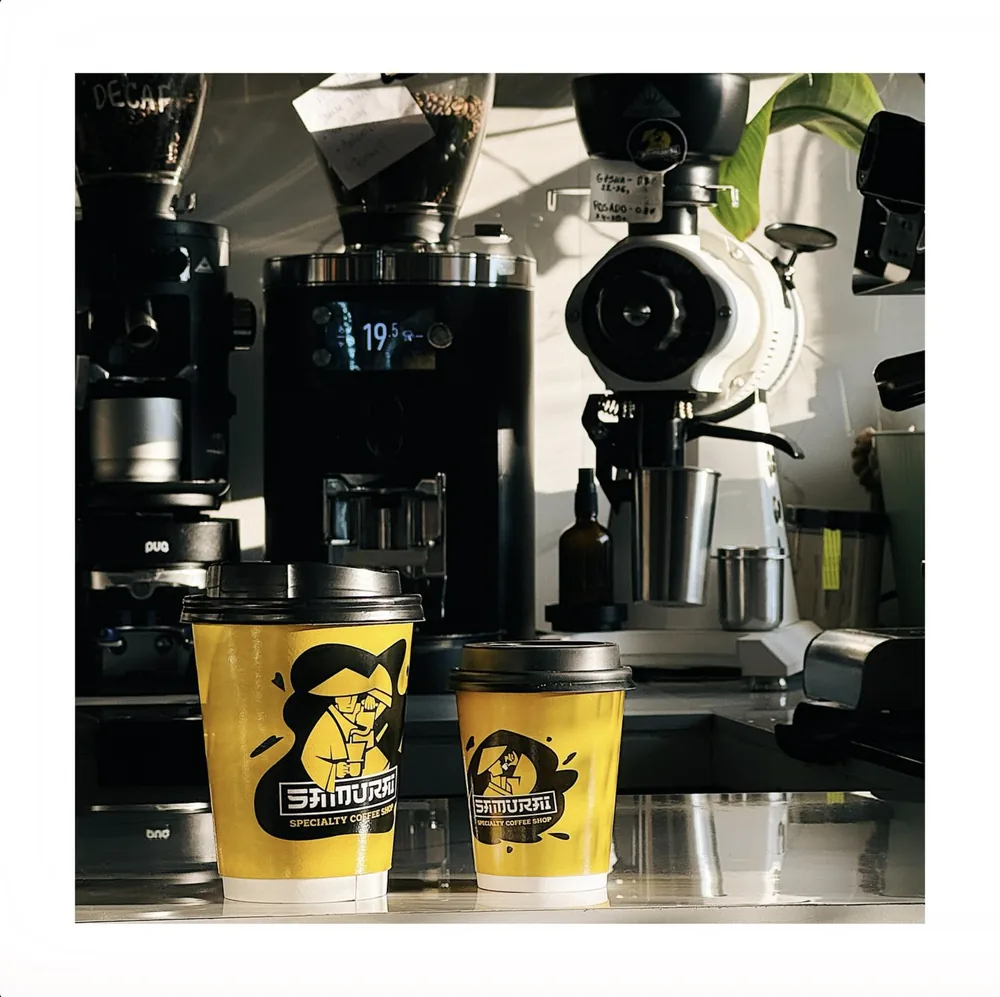 Two branded Samurai takeaway cups on the bar in front of the espresso grinders